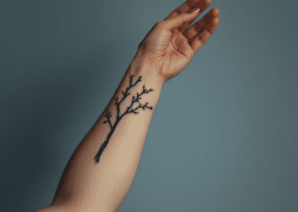 A woman's arm featuring a detailed tattoo of branches with various leaf designs, including a Redwood leaf, Cedar sprigs, and evergreen motifs, showcasing a vintage nature theme.